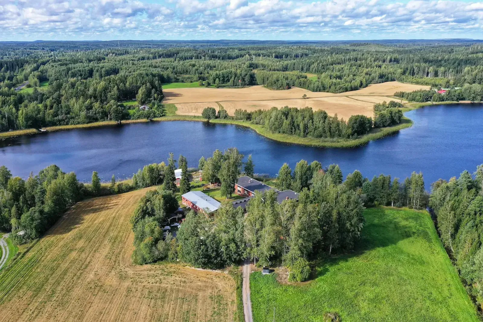 Ilmakuva: Maivitan hoitokeskus järven rannalla peltojen ja metsän keskellä